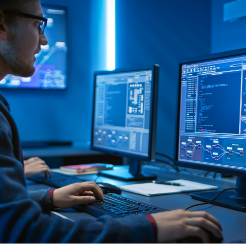 developer sat at desk with two monitors displaying coding